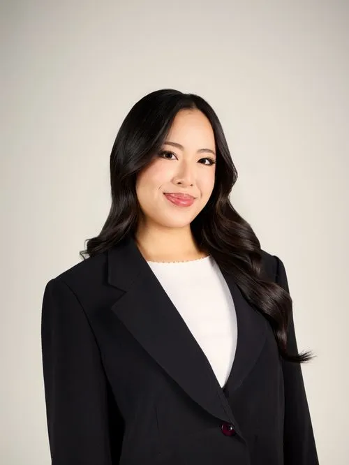Phoebe smiling with long dark hair wearing a black blazer and white top against a light background.